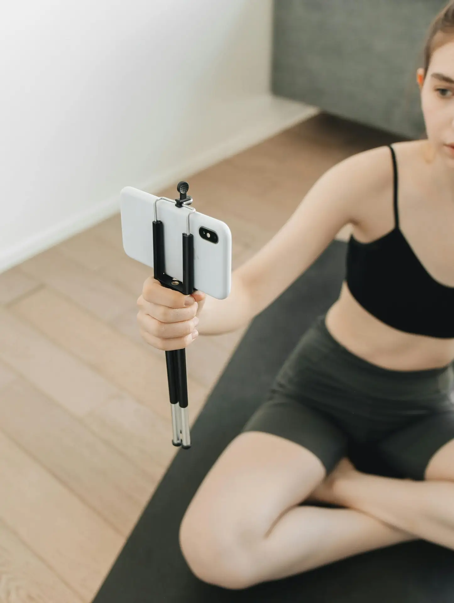 Young woman records yoga practice using smartphone and tripod indoors, emphasizing fitness lifestyle.